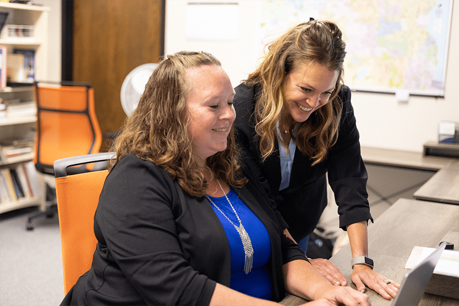 two caucasian women smiling and working at a laptop computer on a desk